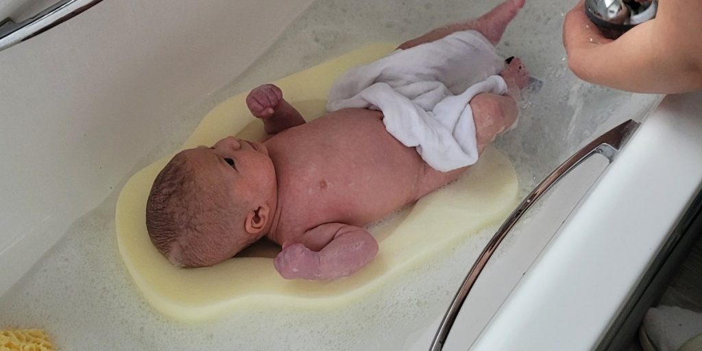 newborn baby on a foam bath support 