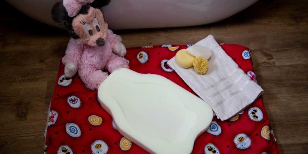 baby bath foam support three bath sponges and a Minnie Mouse toy on a red blanket 